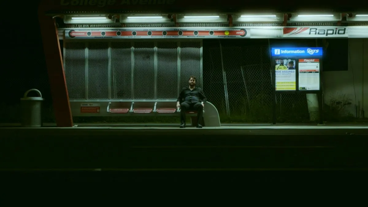 A lone figure at a late-night bus stop, from the short film DEFICIT